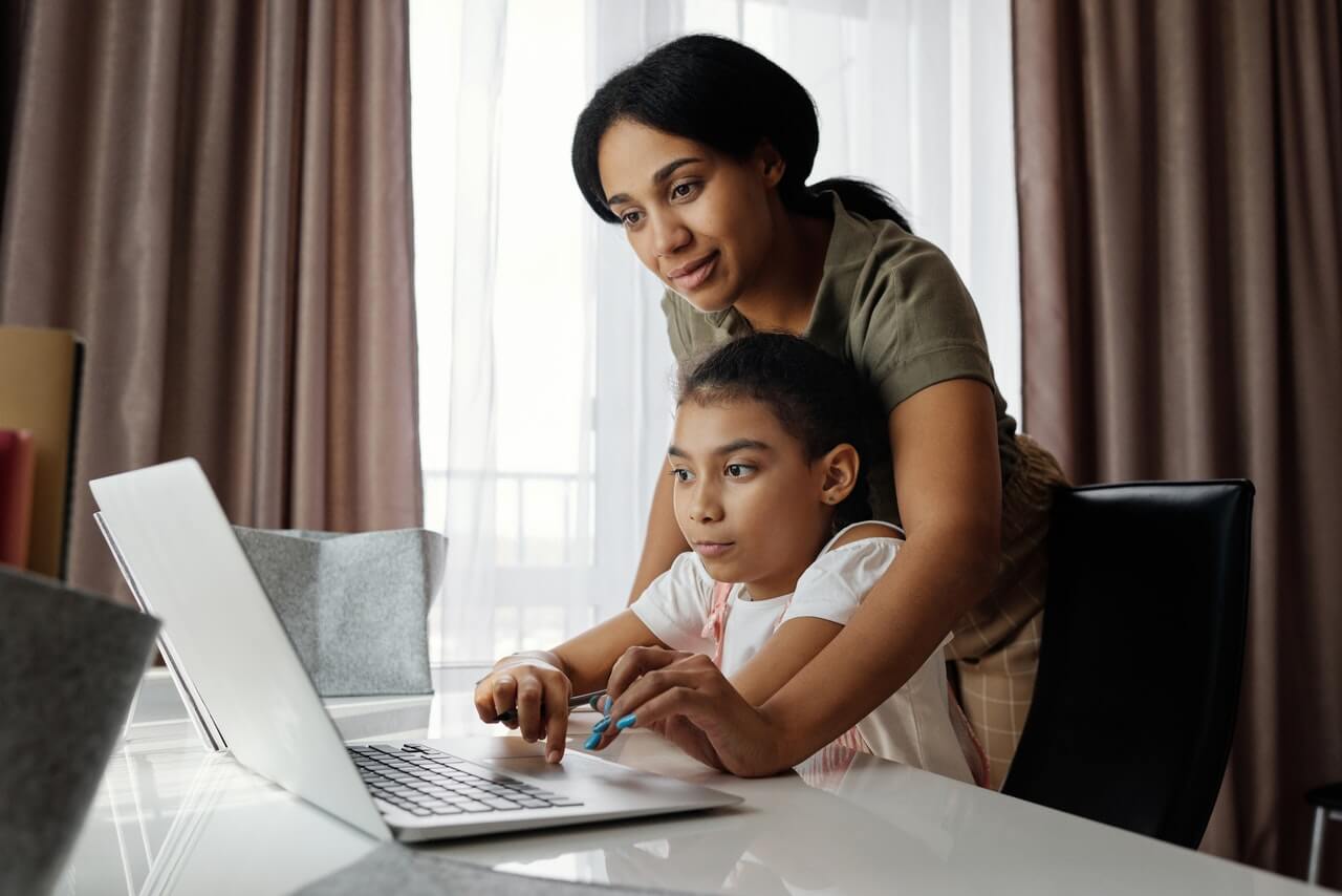 Une maman qui aide sa fille à travailler sur un ordinateur.