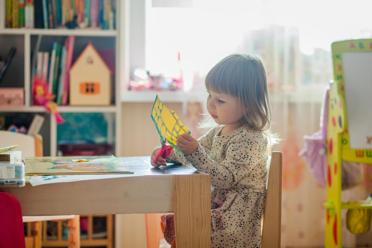 Une jeune fille qui découpe du papier à une table à sa hauteur.