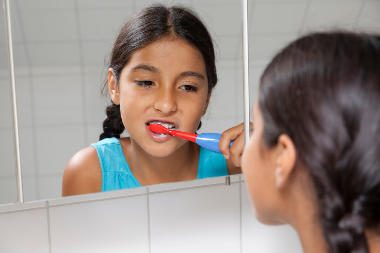 A preteen brushing her teeth while looking in the mirror.