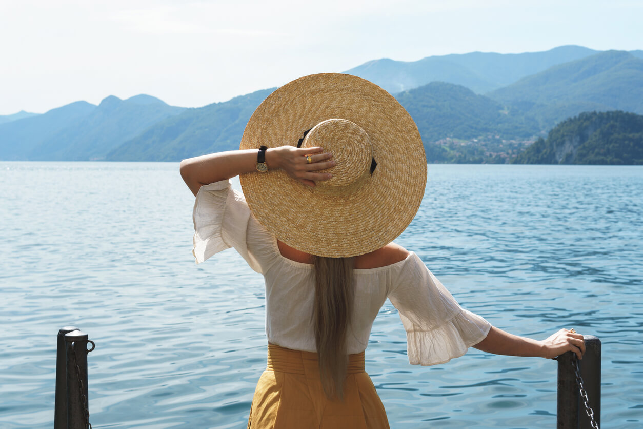 A woman wearing a wide-brimmed hat while looking out on a lake.