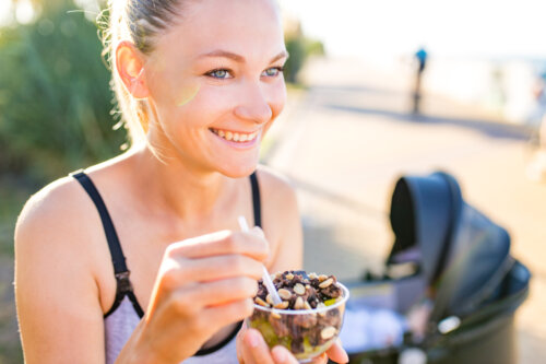 mujer come cereales en el parque con coche de bebe de fondo concepto de posparto