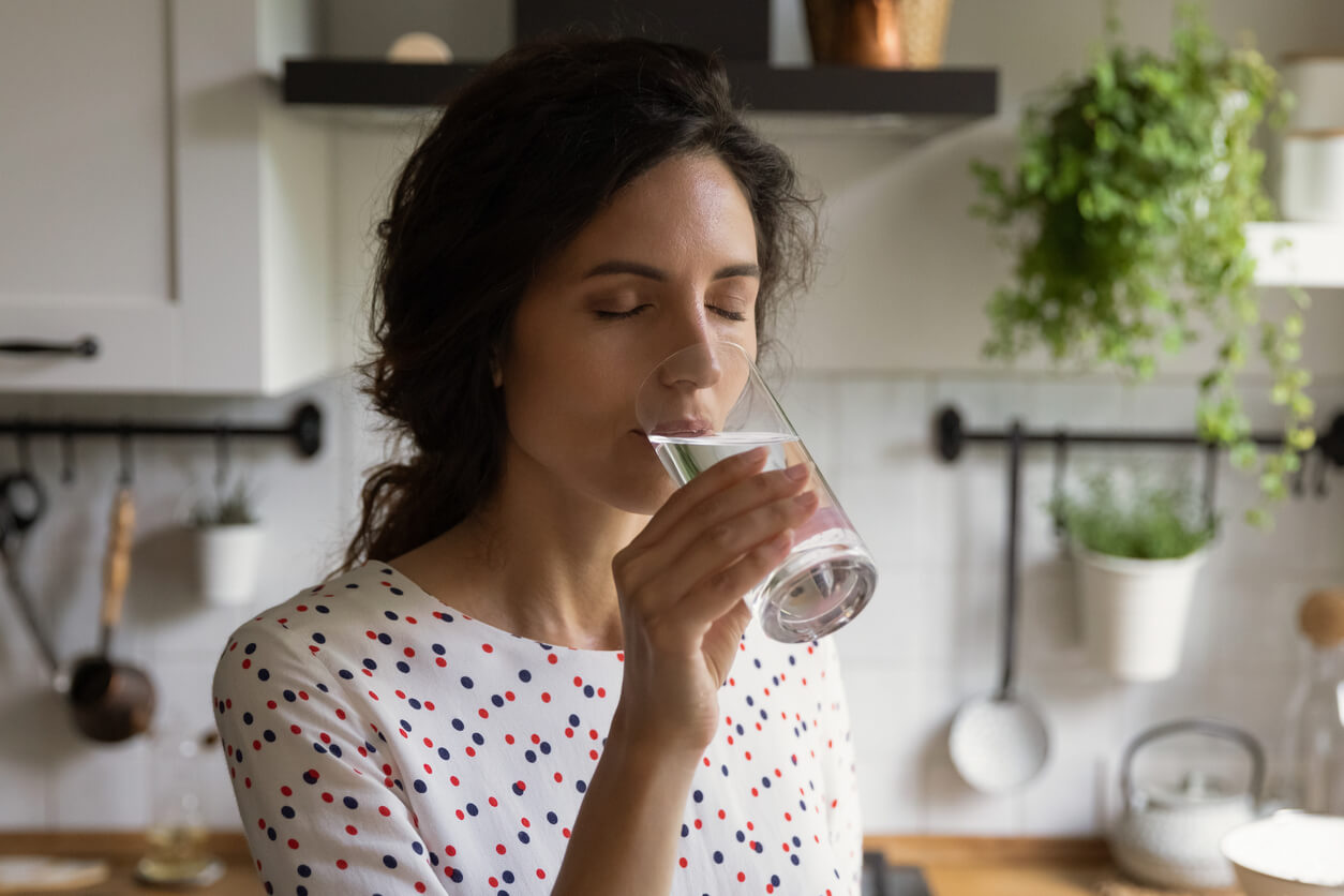 mujer en la cocina bebe agua de vaso de vidrio