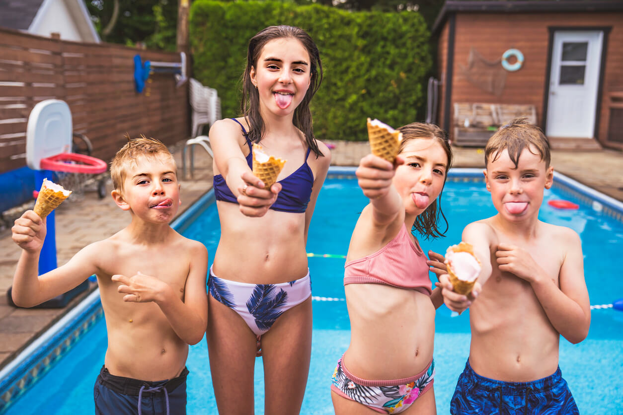 Children eating ice cream cones by a backyard pool.