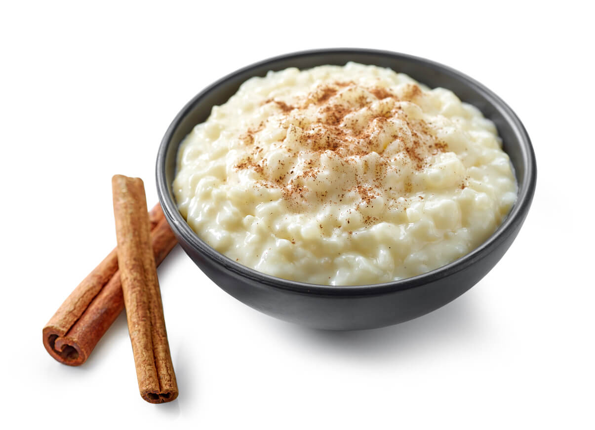 A bowl of rice pudding and two cinnamon sticks.