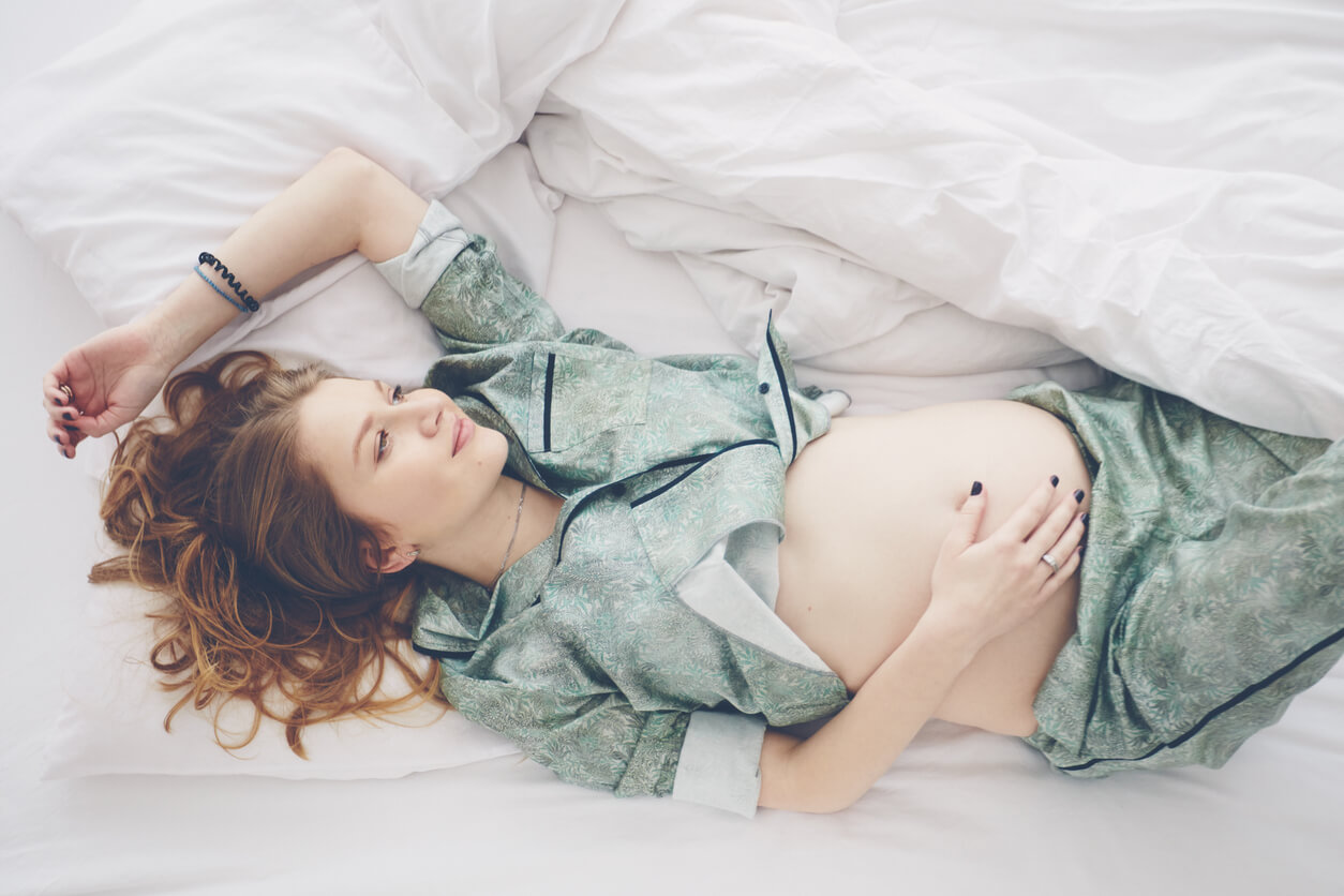 En gravid kvinne som ligger i sengen med hevet arm.