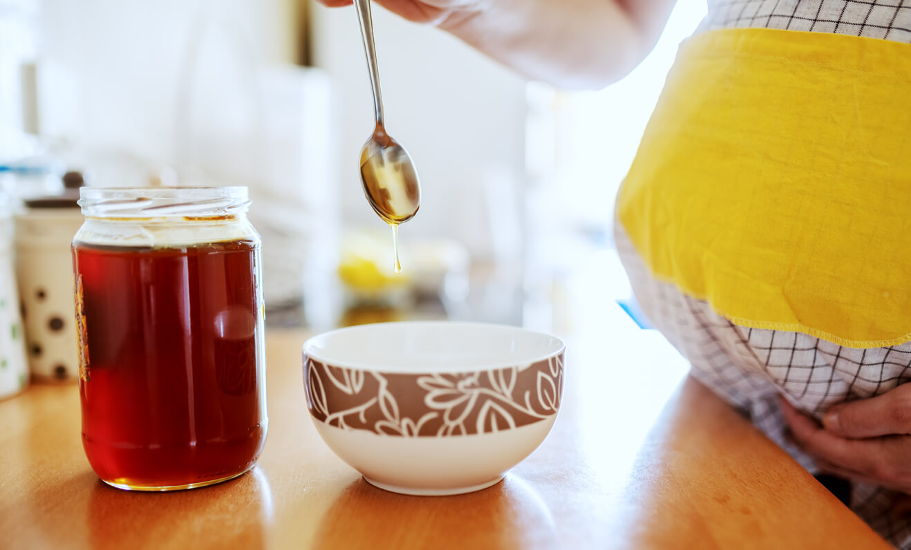 Een zwangere vrouw doet honing in haar thee