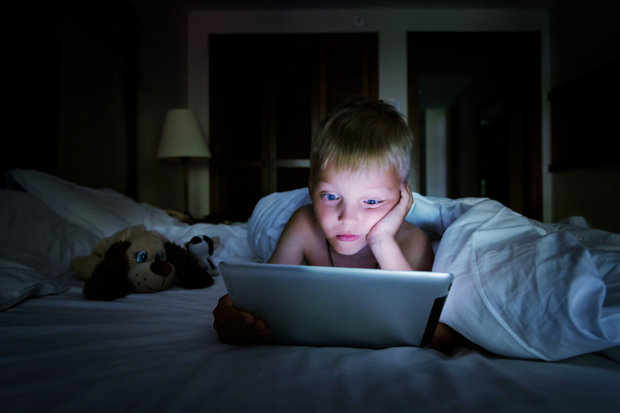 A small boy looking at a tablet in bed at night.