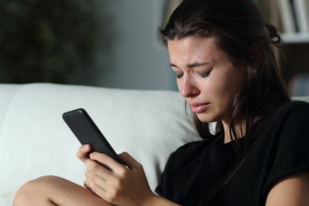 A teenage girl crying whil looking at her phone.