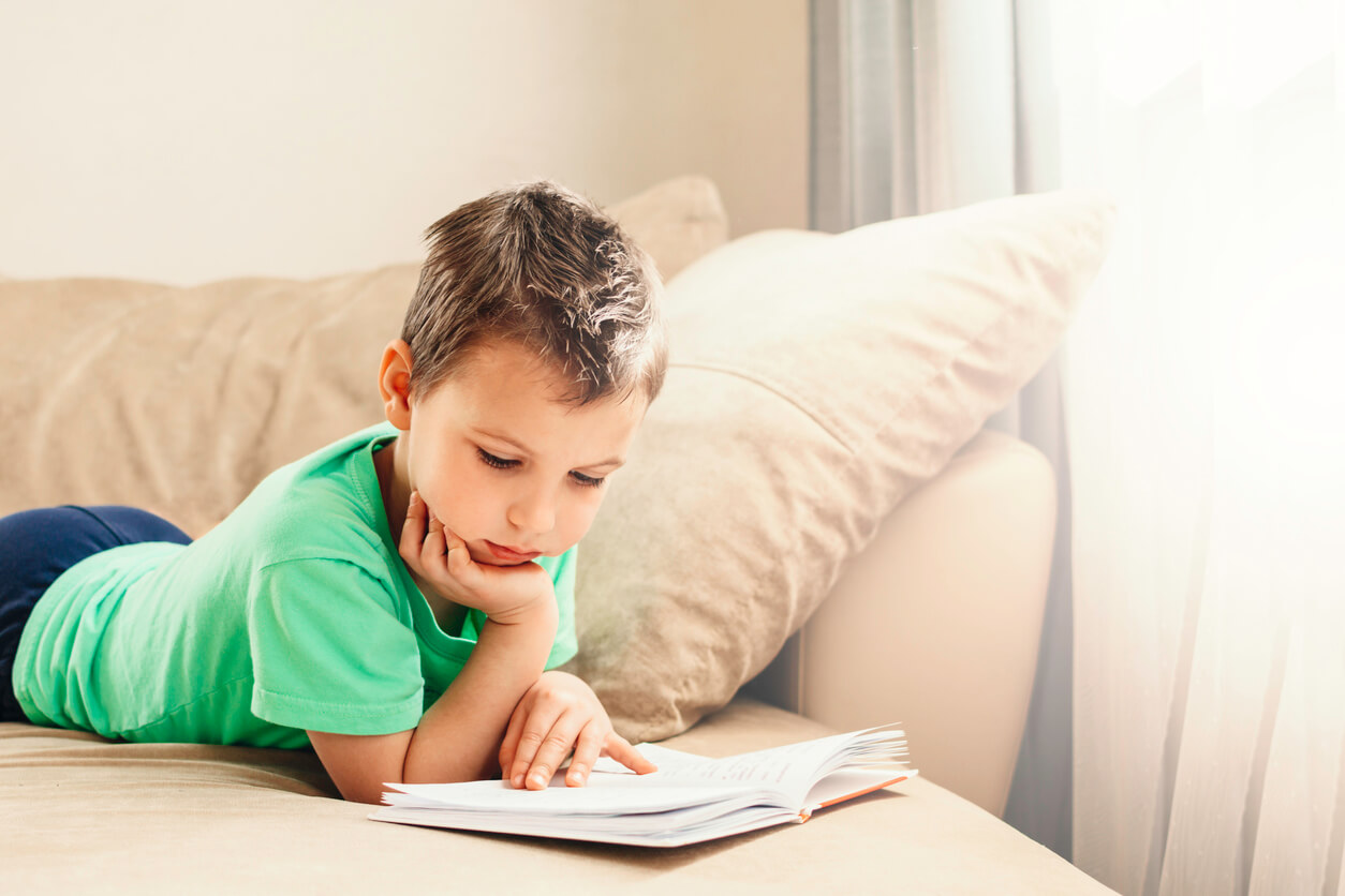 A child lying on the couch reading.
