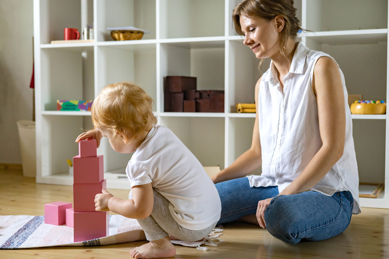 A toddler stacking blocks while her mother watches.