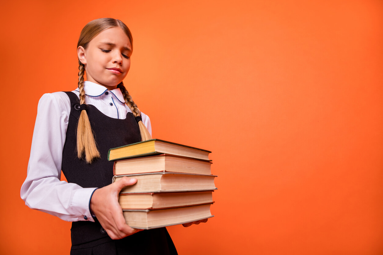 Une jeune fille qui tient une pile de livres dans les bras.