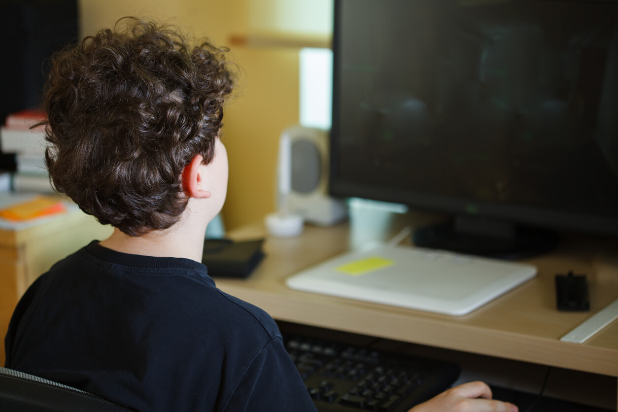 En tenåringsgutt sitter ved et skrivebord ved hjelp av en datamaskin.
