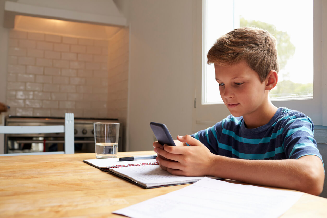 Un enfant qui travaille en regardant son téléphone portable.