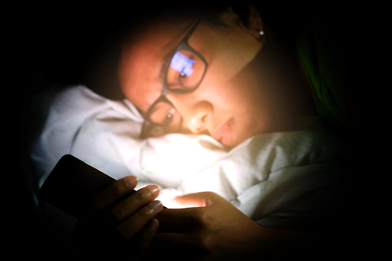 A teen looking at his phone in bed.