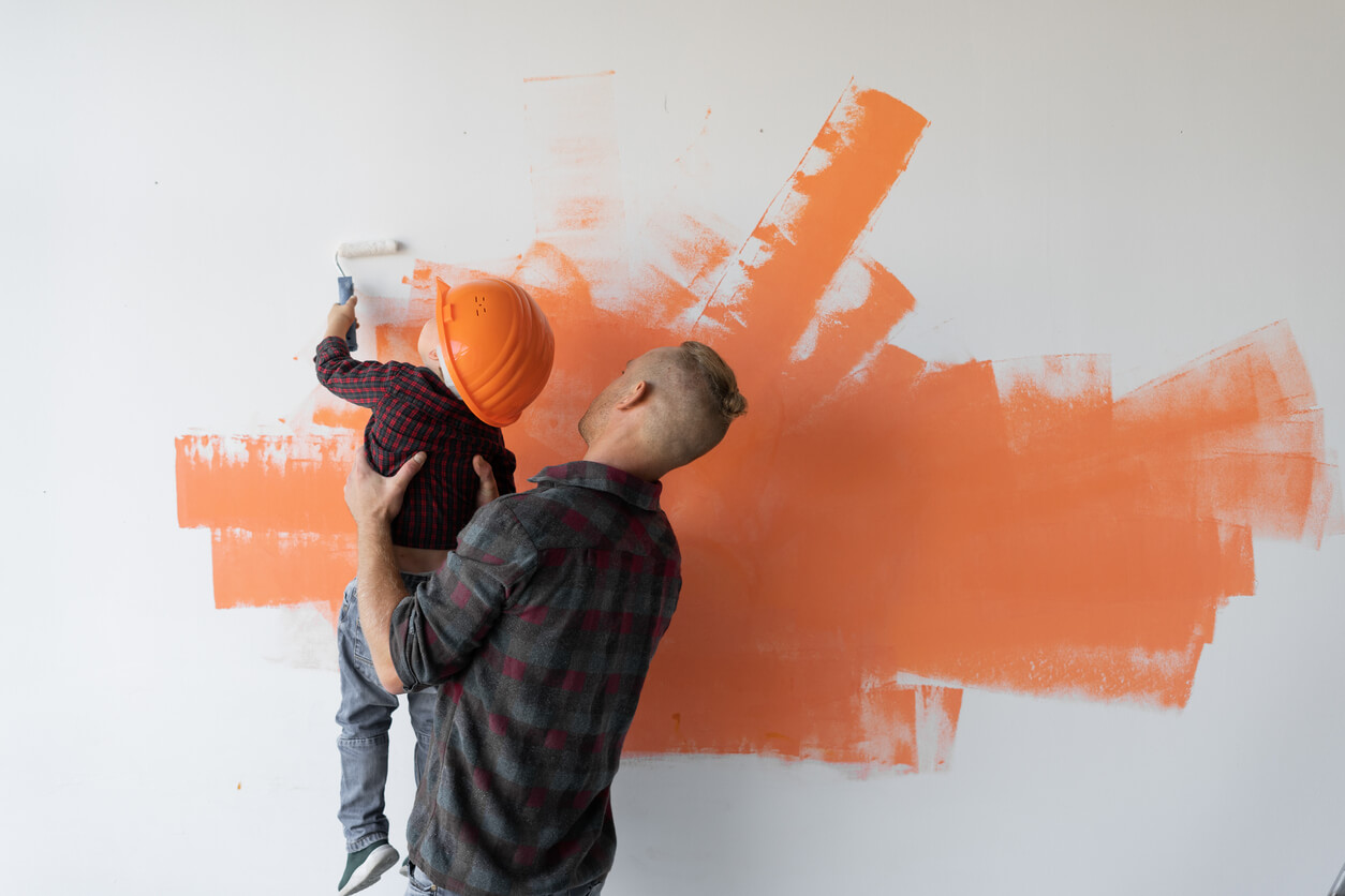 En far lar småsønnen sin hjelpe ham med å male en vegg.