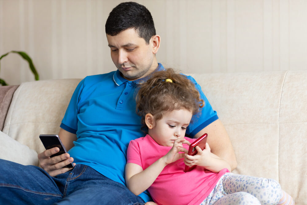 Un père et sa fille sur leur téléphone.