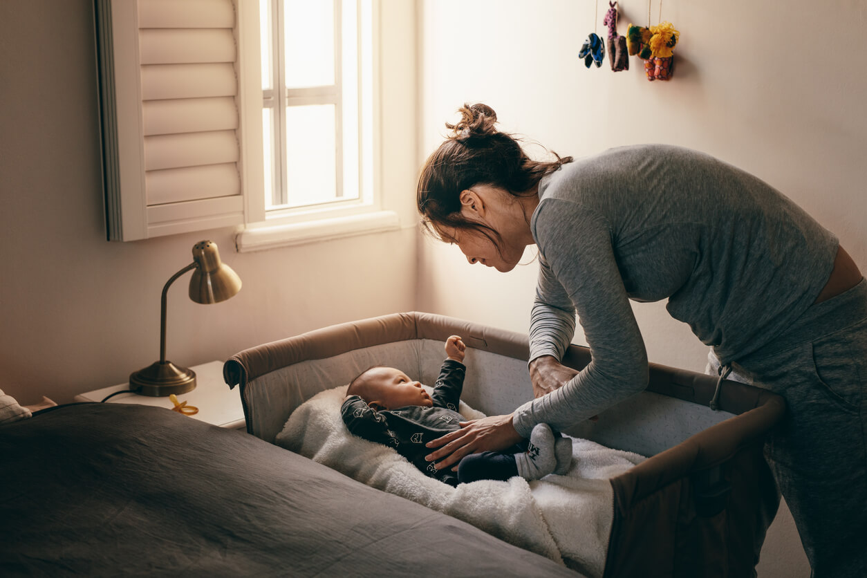 Une maman qui couche son bébé dans son berceau.