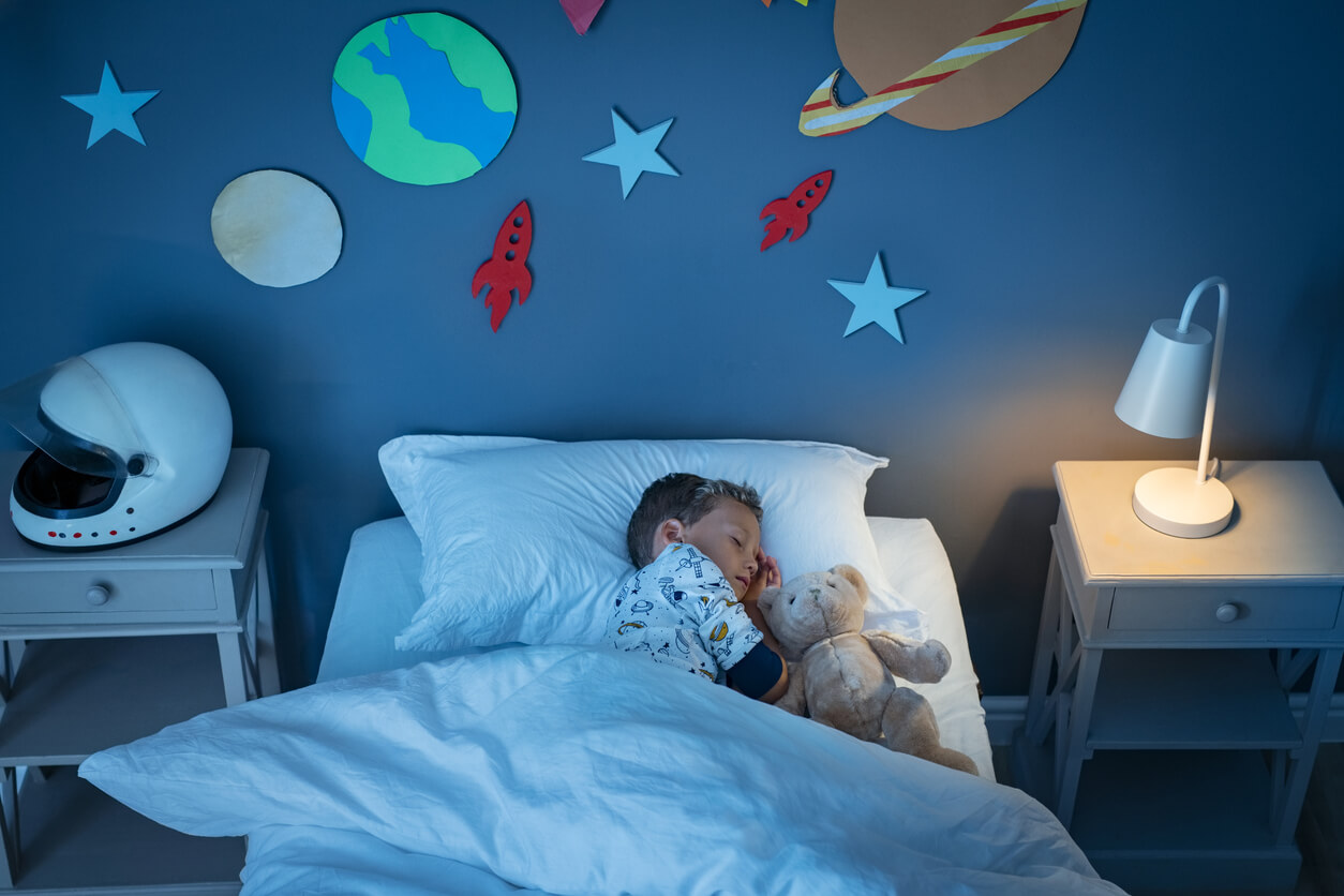 A young boy sleeping in bed with a nightlight on.