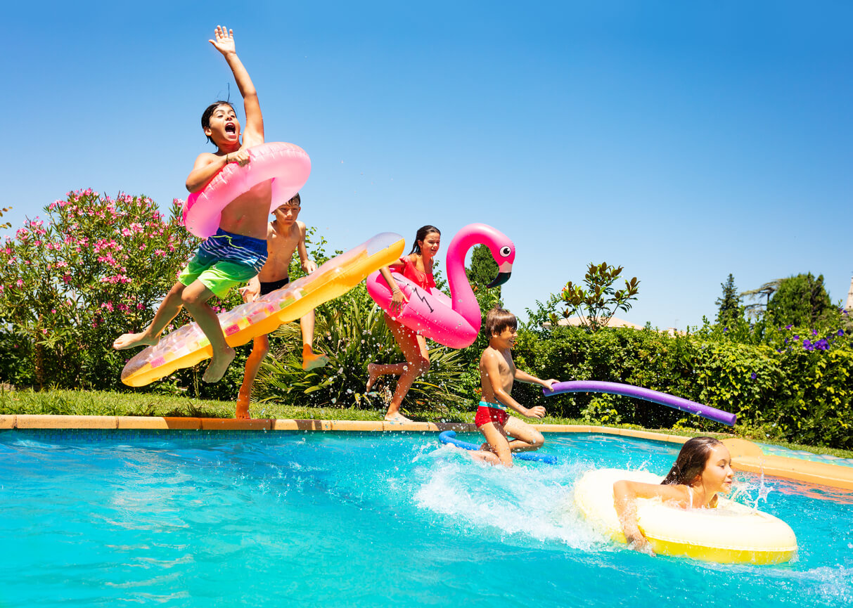 Children jumping into an outdoor swimming pool in the summer.