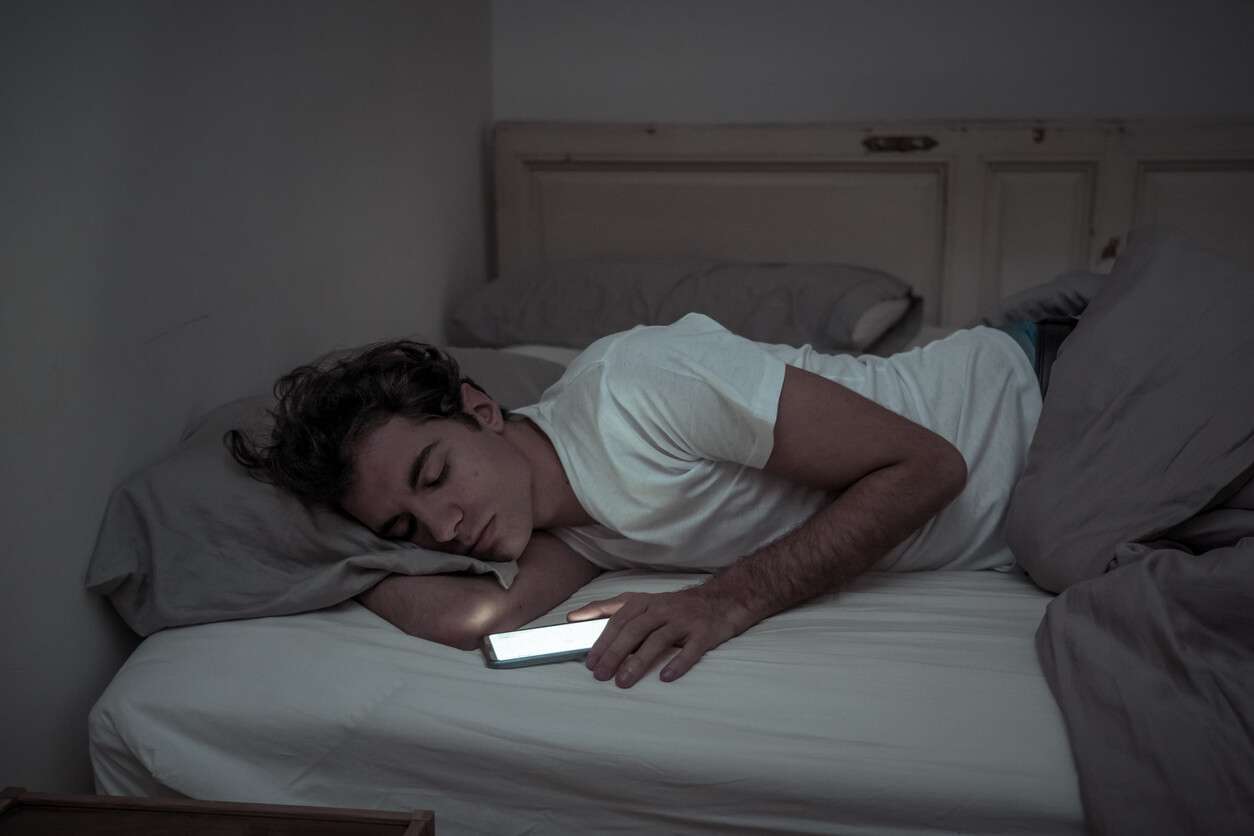 Een tiener slaapt met zijn telefoon nog in zijn hand