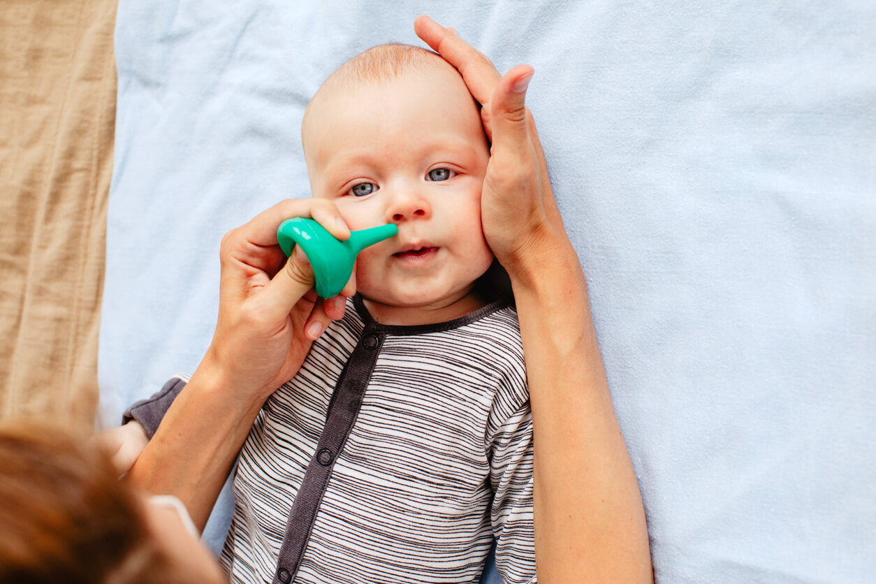En mamma som använder en nasal aspirator på sin bebis.