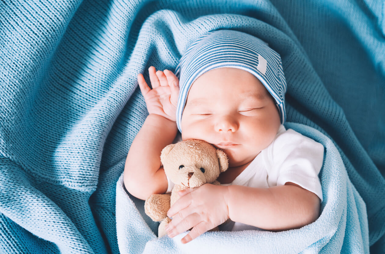 En baby som sover med en bamse.