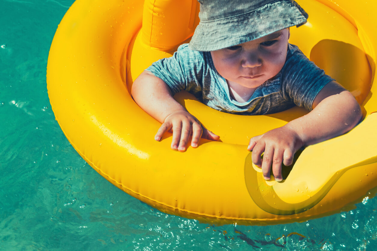 bebe se bana en la piscina en flotador con gorro y remera uv filtro fps