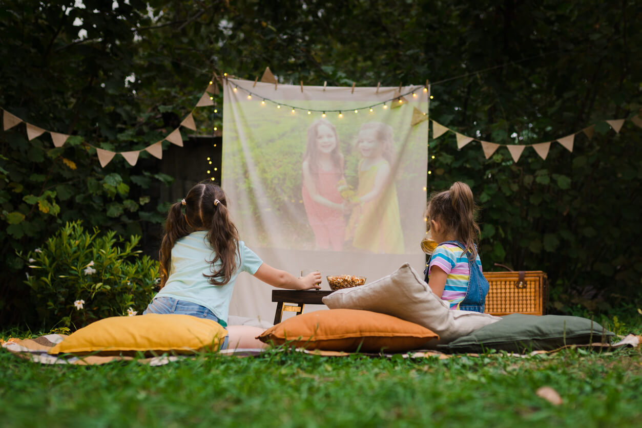 Two little girls eating snacks while watching a movie in their backyard.
