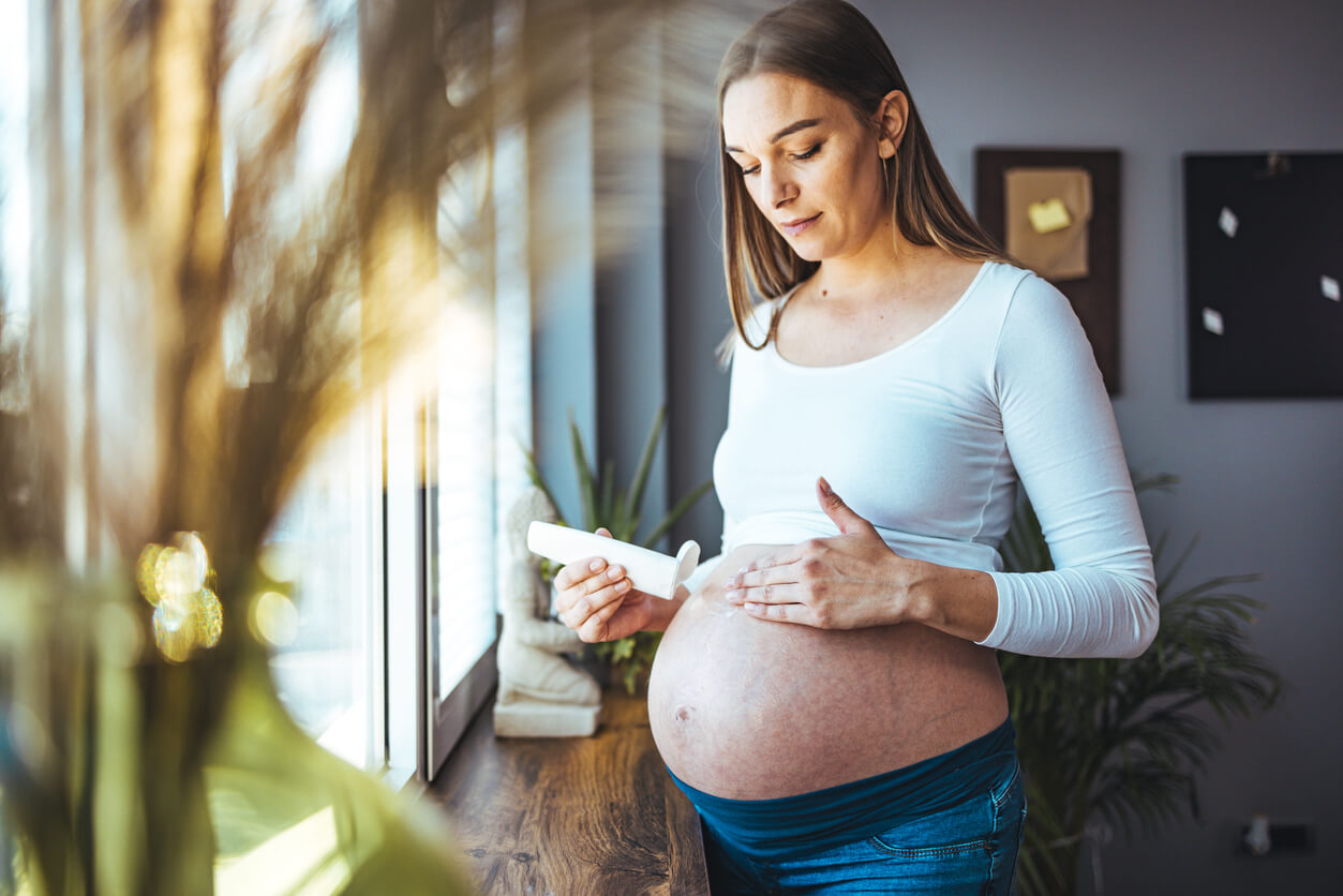 A pregnant woman putting lotion on her belly.