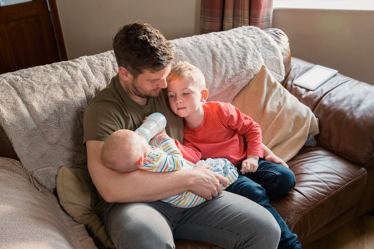 En liten gutt som hjelper faren sin med å mate babybroren sin med flaske.
