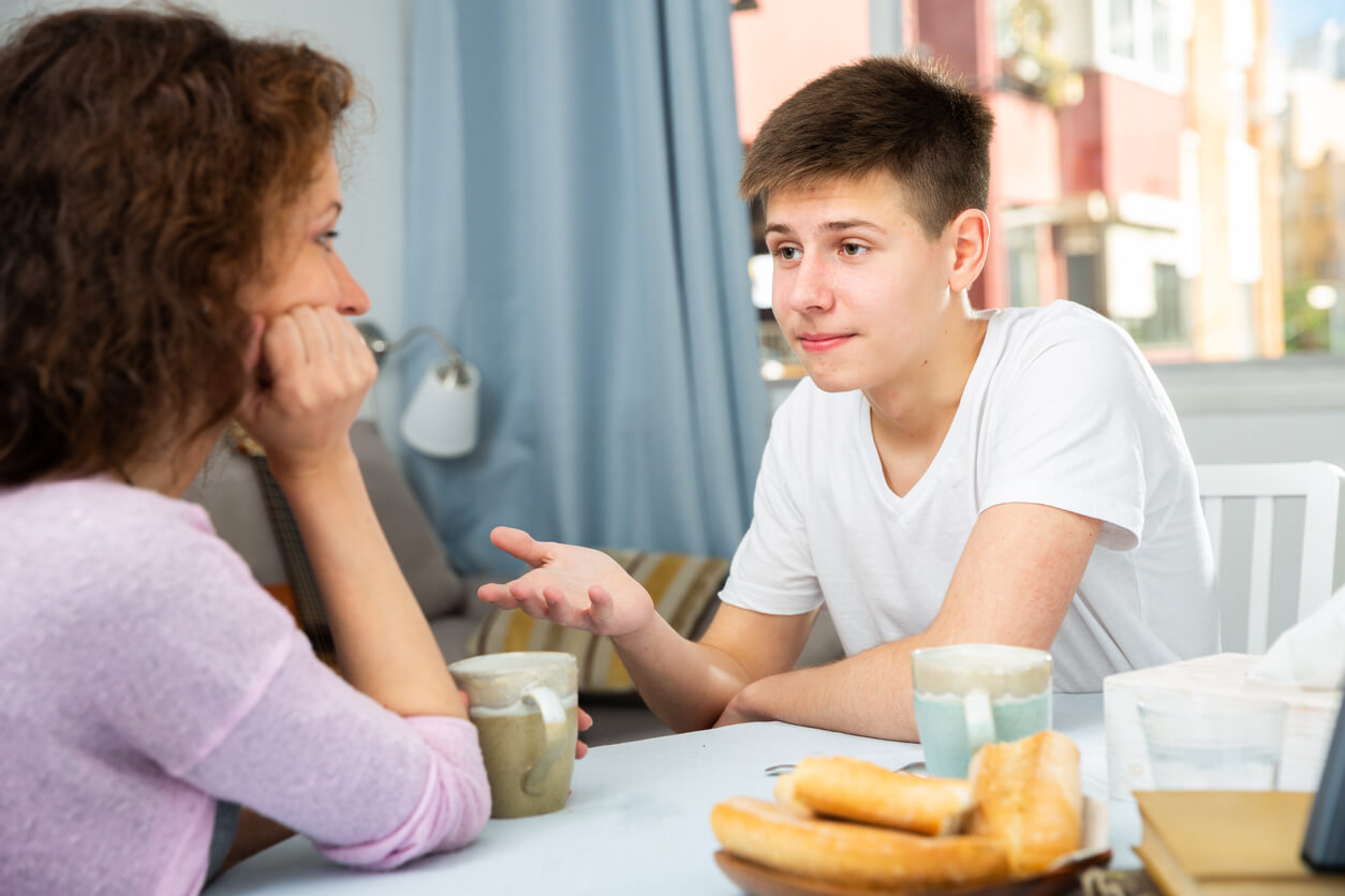 Äiti ja hänen teini-ikäinen poikansa juttelemassa pöydän ääressä.