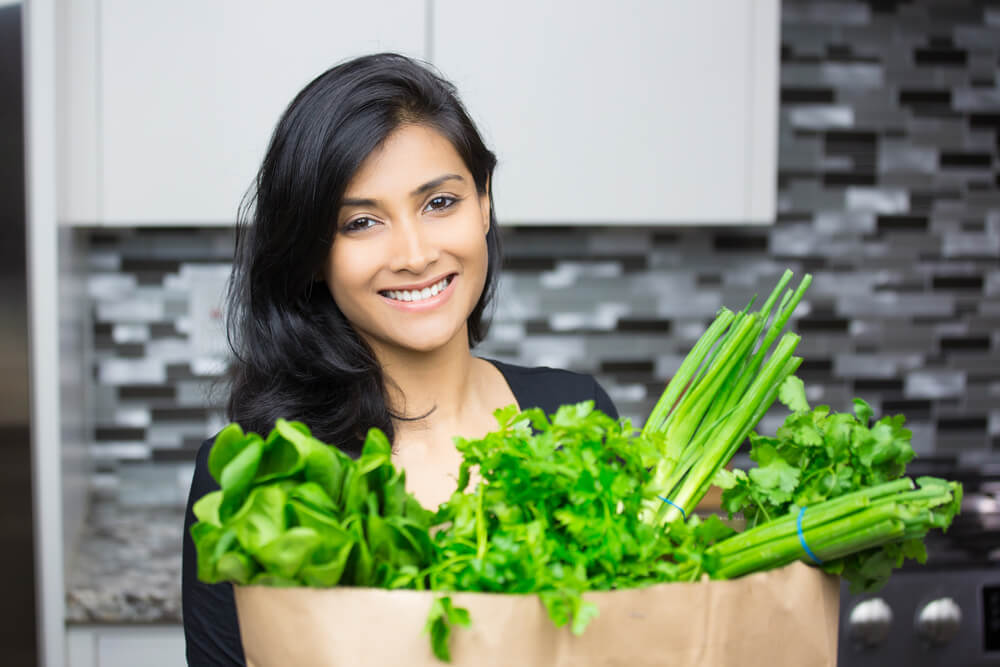 mujer sostiene bolsa de la compra con vegetales hojas verdes acelga espinaca puerro