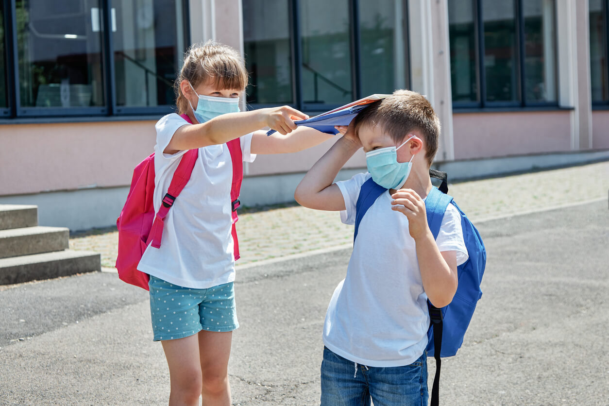 An elementary school girl hitting a younger boy on the head with notebooks.