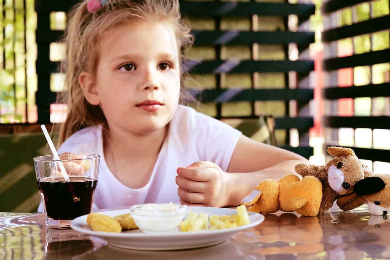 A child eating nuggets and fries with a glass of coke.