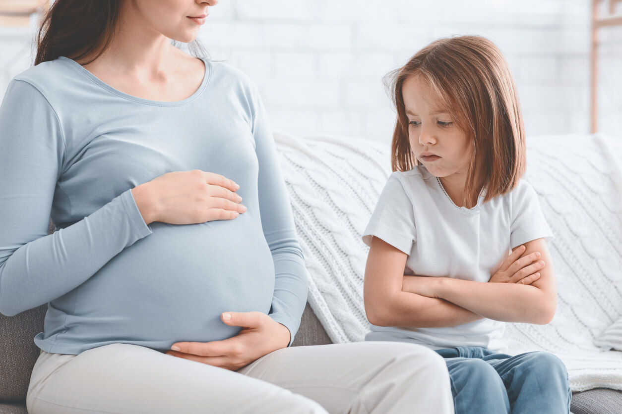 En liten flicka stirrar argt på sin mammas gravida mage.