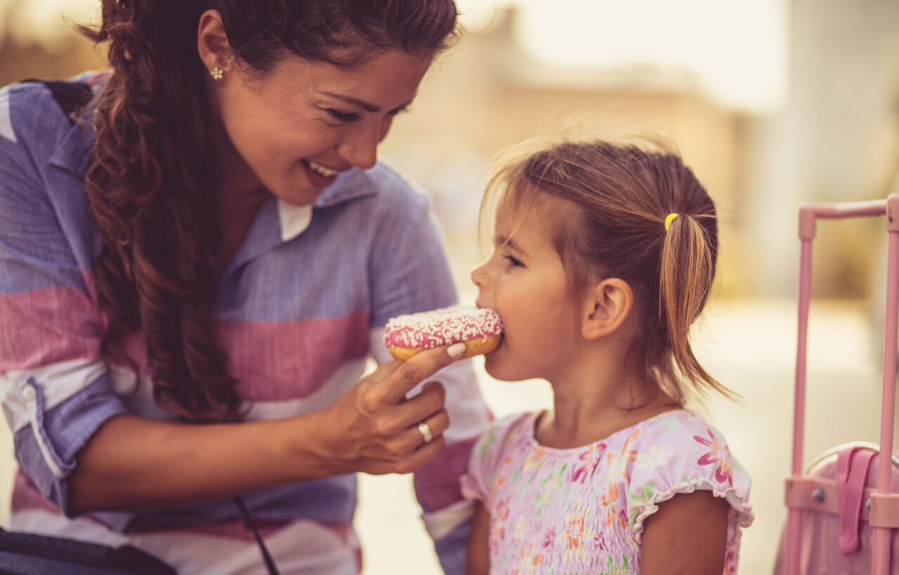 A mother feeding her young daughter a sprinkled donut.