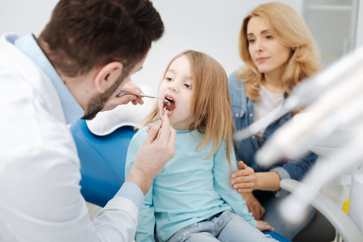 En tandläkare tittar på en liten flickas tänder.
