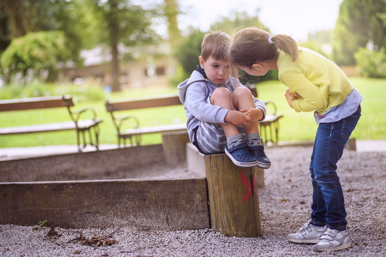 En liten jente bøyde seg for å snakke med en mindre gutt krøllet sammen på en stubbe i en park.