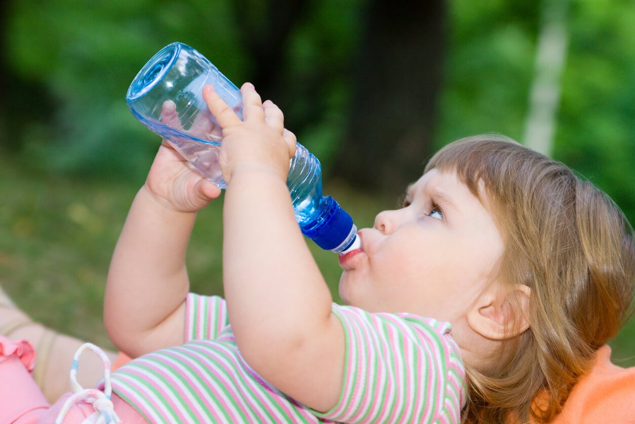 A little girl drinking from a water bottle while lying in the grass.