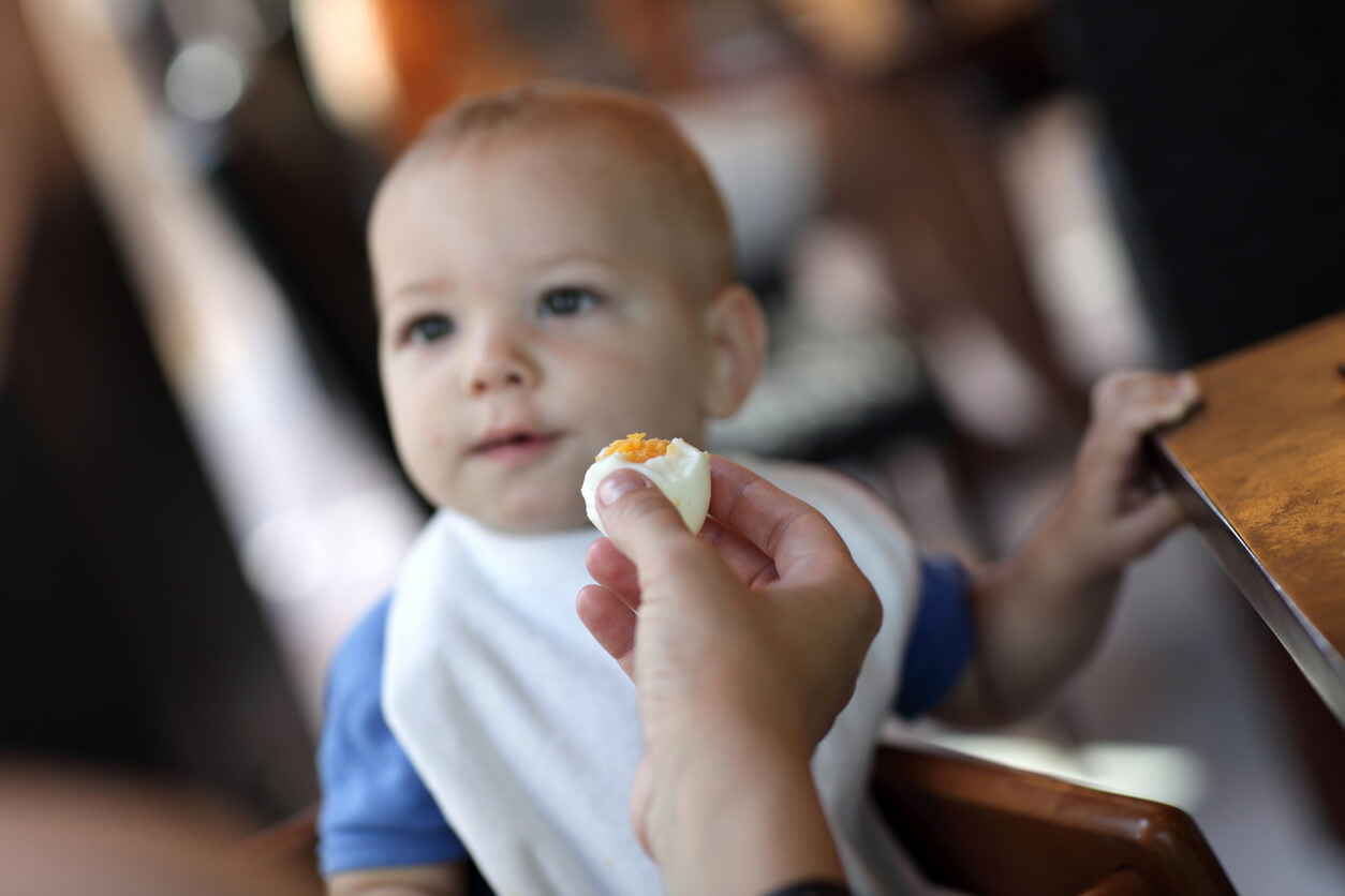 A person offering a boiled egg to a baby.