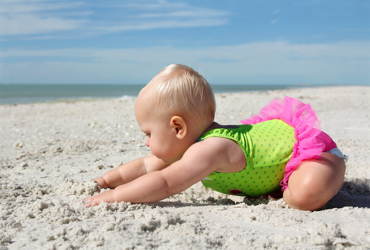 A baby playing in the sand on the beach.
