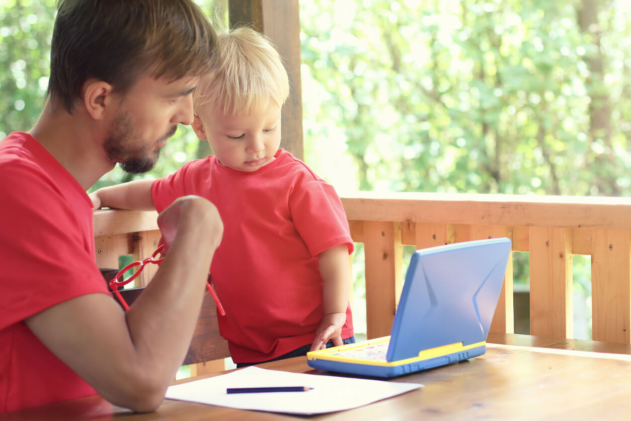 A toddler and his dad sitting at an outdoor table and learning with a toy laptop computer.