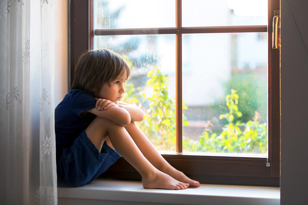 Un enfant assis seul au bord d'une fenêtre.