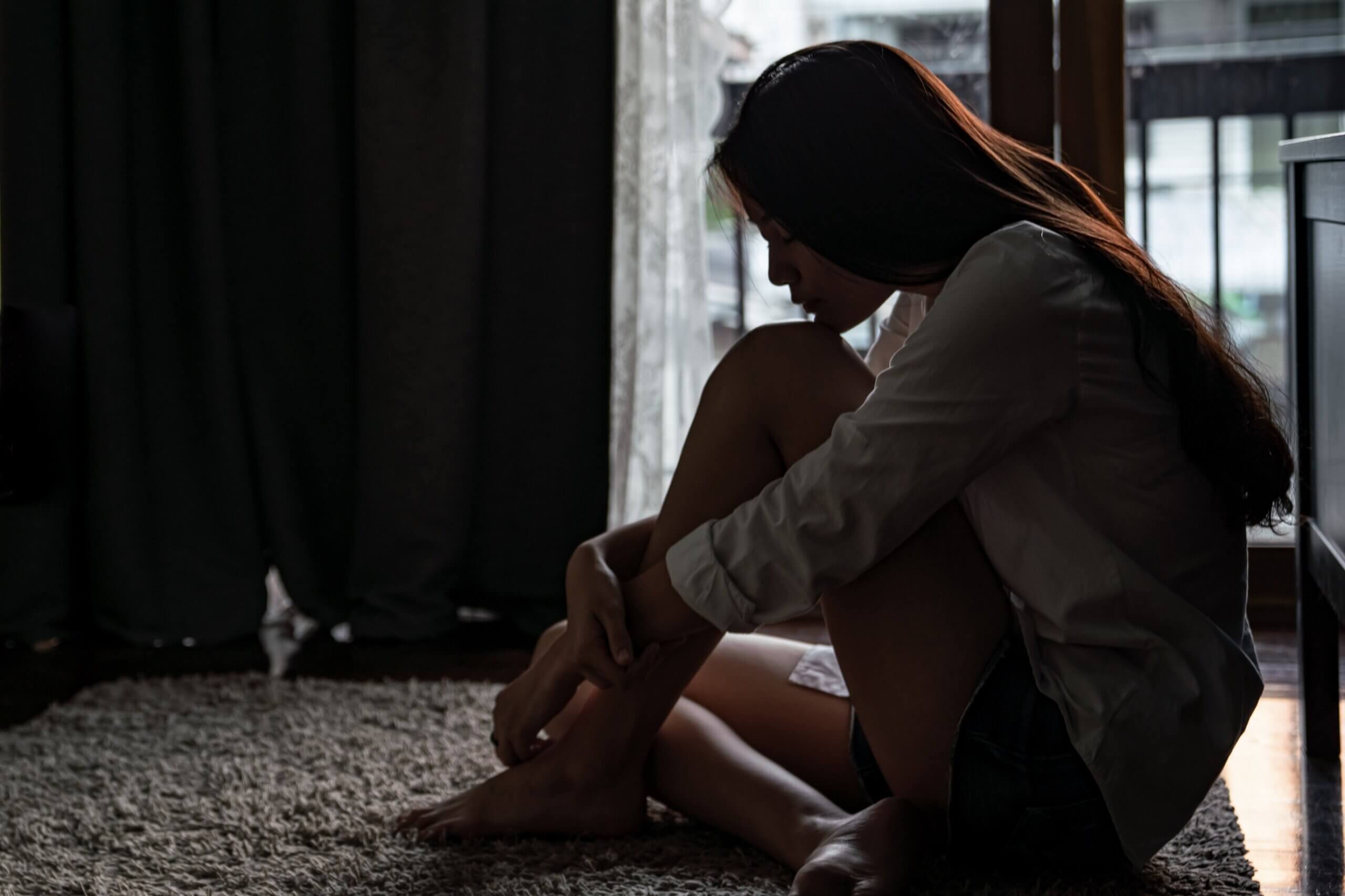 A teenage girl sitting on the floor in the dark.