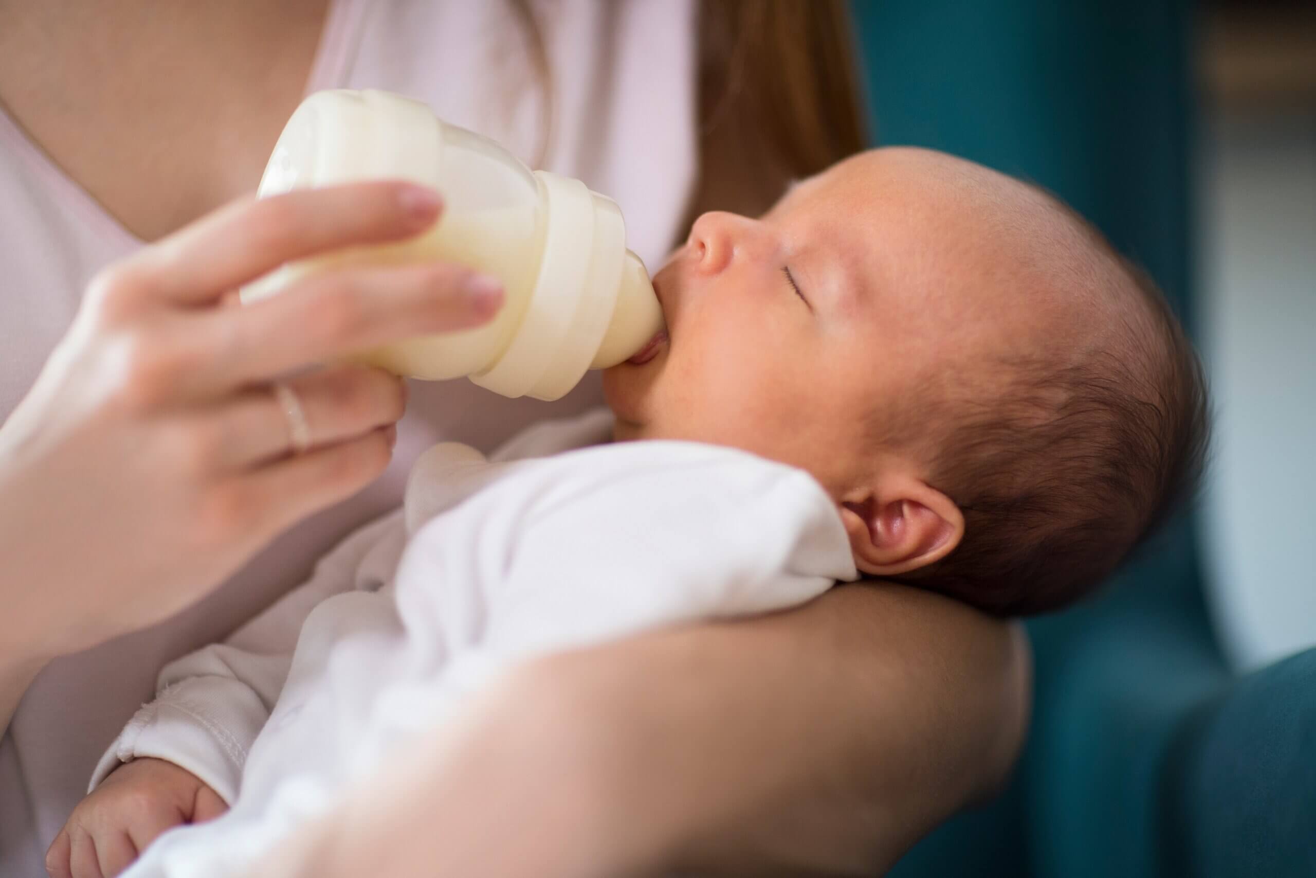 A sleeping newborn drinking from a bottle.