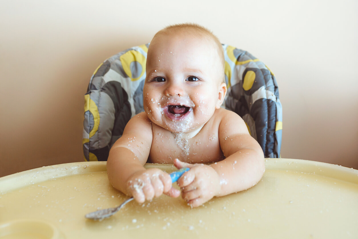 A baby sitting in a high-chair, covered in baby food.