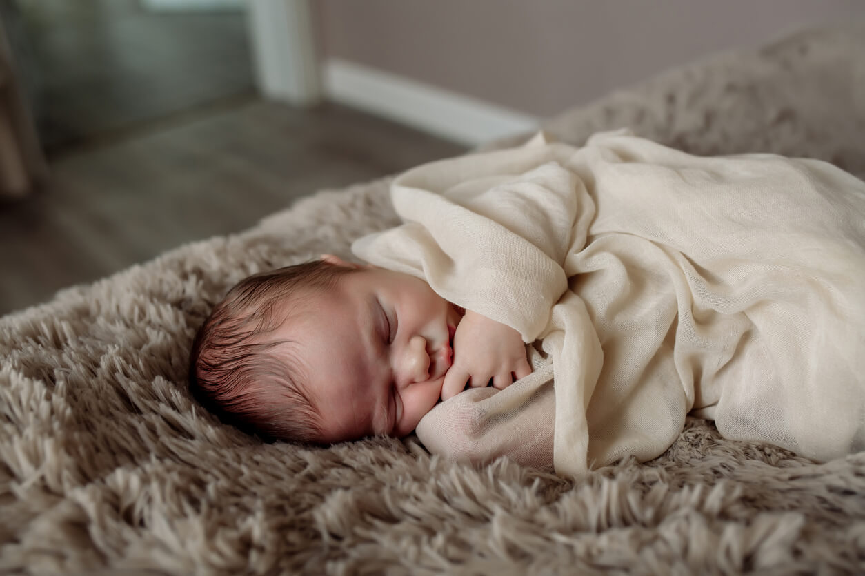 En nyfødt som sover pakket inn på en seng.
