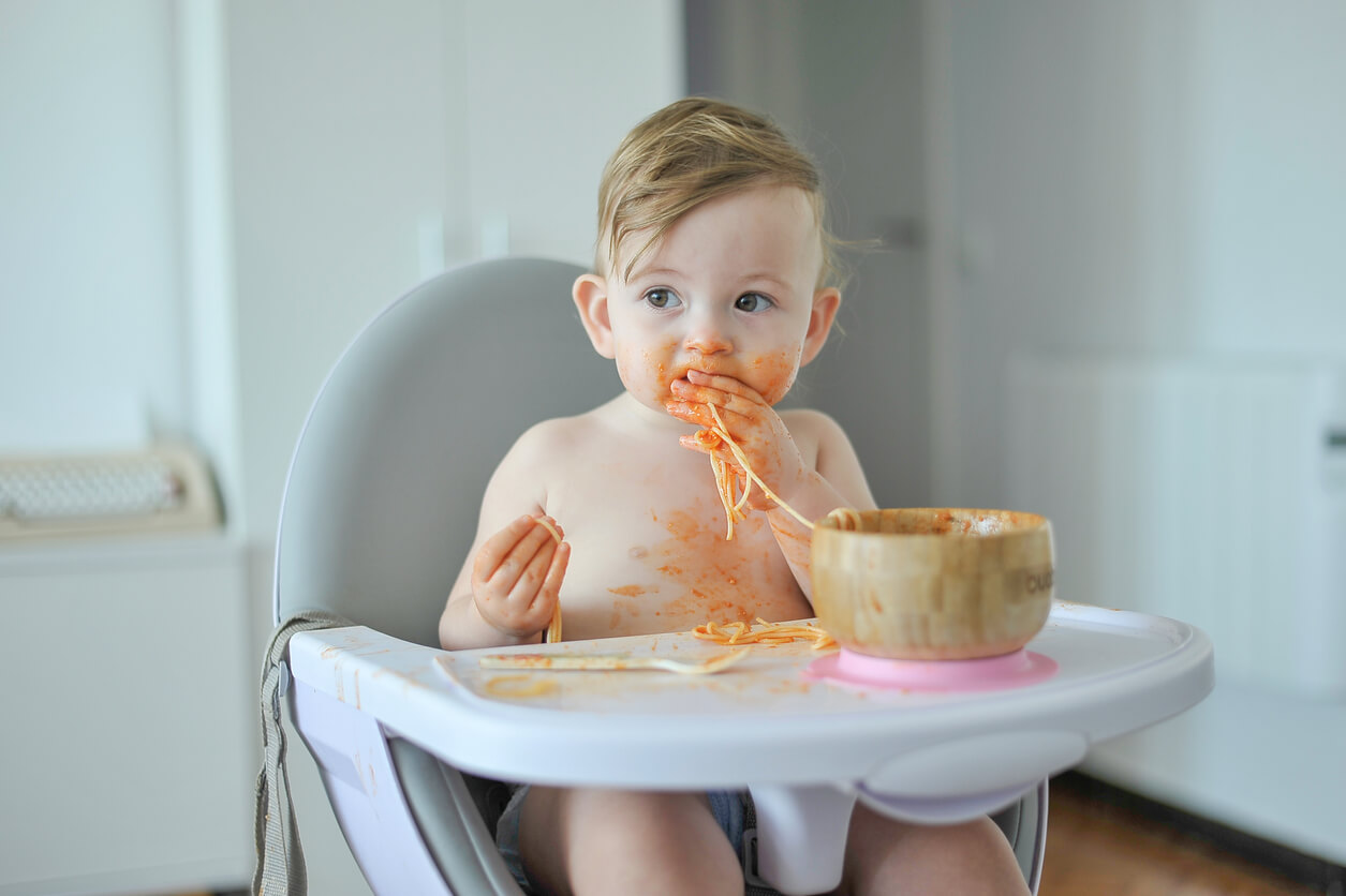 A baby eating pasta with his hands.