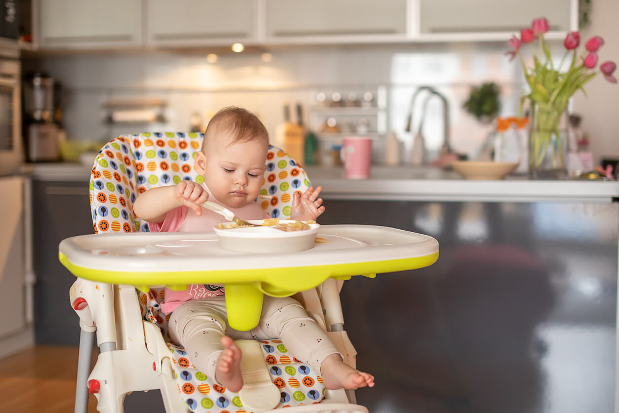 A baby girl sitting in a highchair eating on her own.