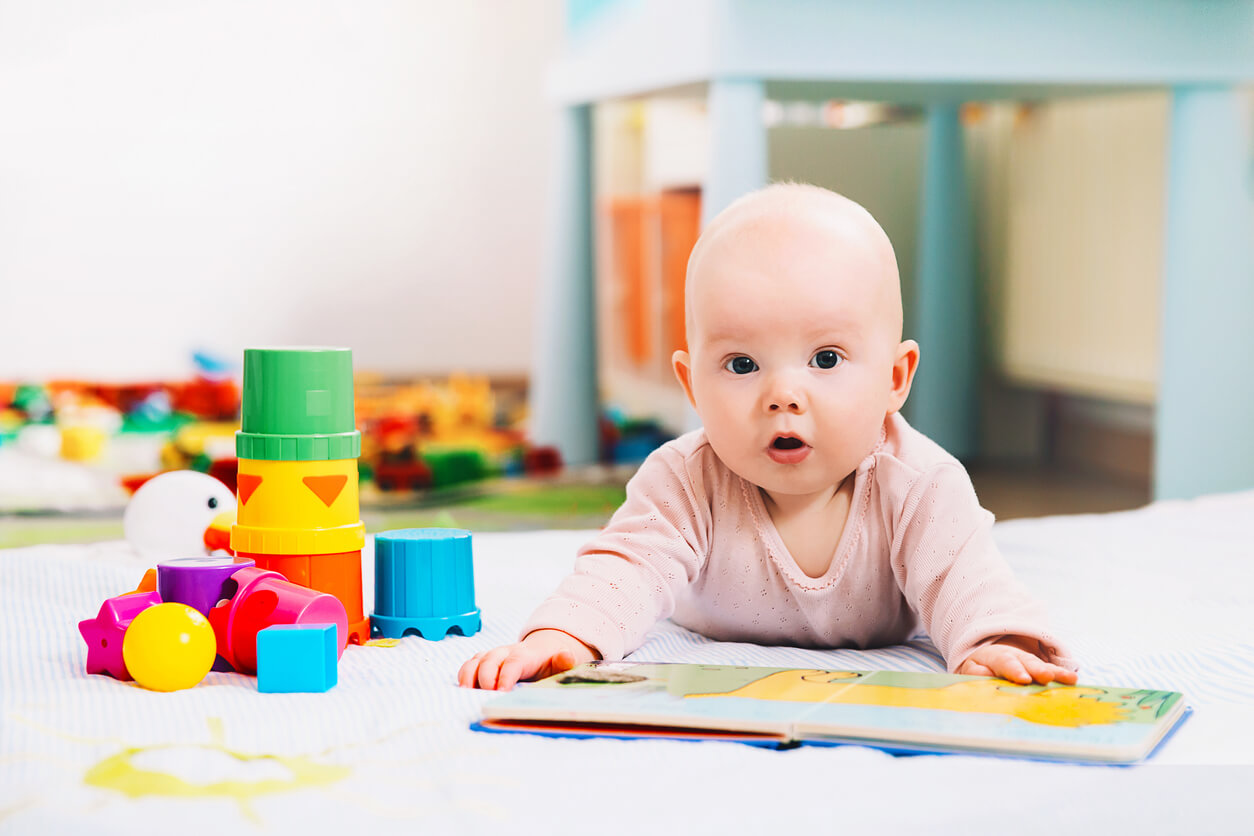 Un bébé allongé sur le ventre avec un livre dans les mains.